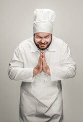 Bearded overweight male in chef uniform folding hands in gratitude and looking at camera while...