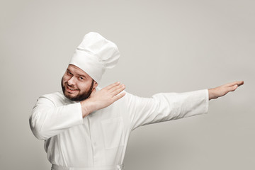 Bearded professional cook smiling and making dab movement while standing on light gray background...
