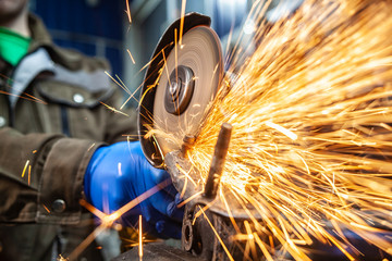 Close-up of a man sawing   bearing metal with a hand circular saw, bright flashes flying in...