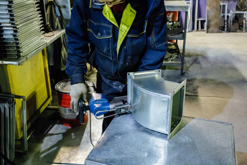 Worker in metalworking plant installing rivets into part for construction ducts of industrial air...