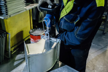 Worker in metalworking plant installing rivets into part for construction ducts of industrial air...