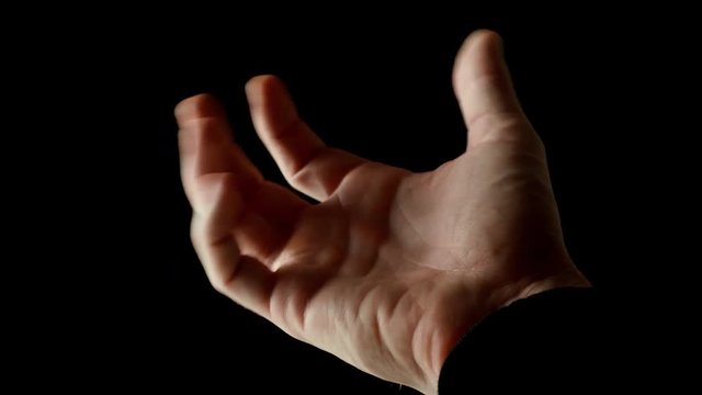Human male palm in the rays of light isolated on black background. A man shows an open hand, then slowly clench his fingers into a fist and again unclenched. Stock video slow motion