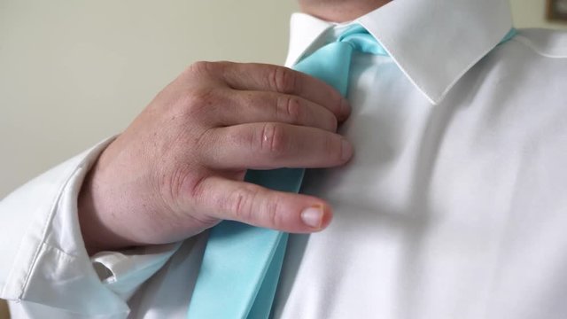 Businessman man puts on blue tie with his hands to white shirt in morning going to work. Concept of business employee. Dress code. Close-up.