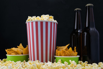 red and white paper cup and containers with nachos on popcorn on a black background