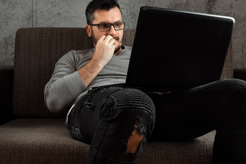 A man watches an adult video on a laptop while sitting on the couch. The concept of porn, men's...
