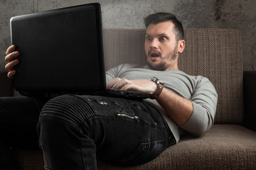 A man watches an adult video on a laptop while sitting on the couch. The concept of porn,...