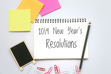 Text 2019 new year's resolutions on notepad with pencil and sticky note on white background,office desk.