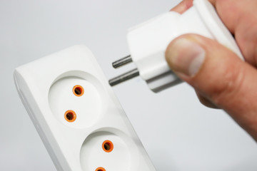 Closeup of a man's hand inserting plug into electrical outlet