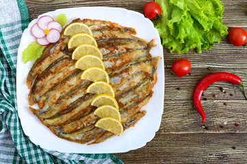 Baked capelin on a white plate on a wooden table. A dish of small fish. Top view.