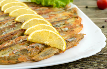 Baked capelin on a white plate on a wooden table. A dish of small fish