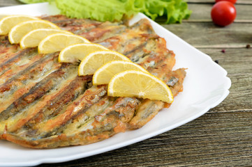 Baked capelin on a white plate on a wooden table. A dish of small fish