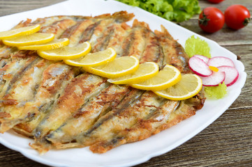 Baked capelin on a white plate on a wooden table. A dish of small fish