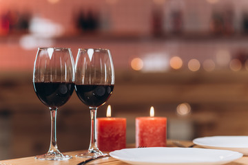 Two glasses with red wine and burning candles on a served table close-up. Romantic atmosphere, blurred background