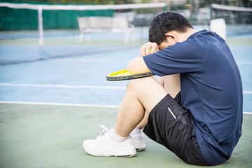 Sad tennis player sitting in the court after lose a match - people in sport tennis game concept
