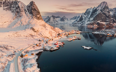 Aerial view of Scandinavian village on coastline in snowy valley at sunset
