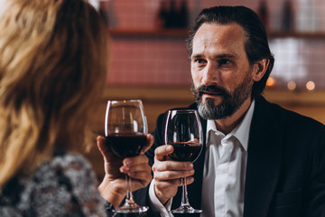 Middle-aged man look at the woman and raises a glass of red wine with her