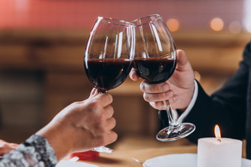 Couple in love raises glasses of red wine, focus on glasses close-up, blurred background