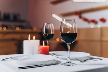 Two glasses with red wine and burning candles on a served table close-up, blurred background