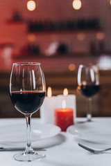 Two glasses with red wine and burning candles on a served table  close-up. Focus on one glass, blurred background