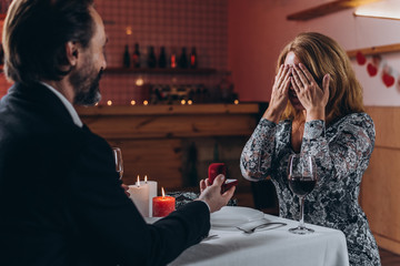 A middle aged man makes a marriage proposal to a woman at dinner. Woman covered her face with her hands