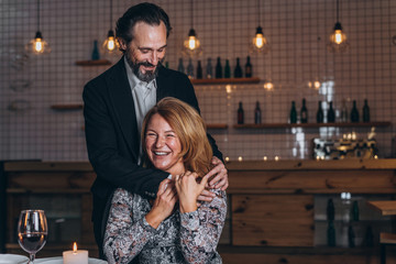 Man stands next to a woman in a restaurant and hugs her from behind.