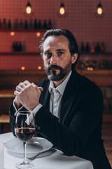 Lonely bearded man sits alone with a glass of wine at a table in a restaurant.