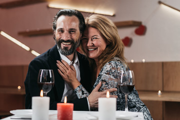 A happy man and woman are sitting and hugging in a restaurant.