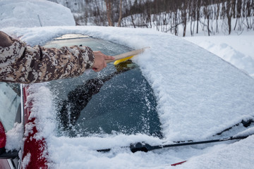Hand using brush sweeping snow on car windscreen