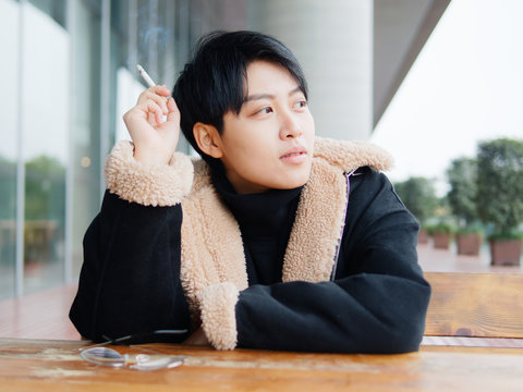 Portrait of cute beautiful young lesbian with short haircut and trendy boyish clothes sitting outside with cigarette in hand, cool Chinese gay girl.