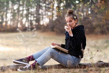 Girl reading a book and having cup of coffee outdoors