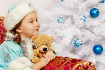 Little girl in the snow maiden costume with a teddy bear near th