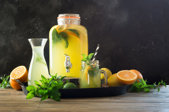 Lemonade with orange, lemon and mint in different mason jar on black and wooden board. Summer healthy detox drink.