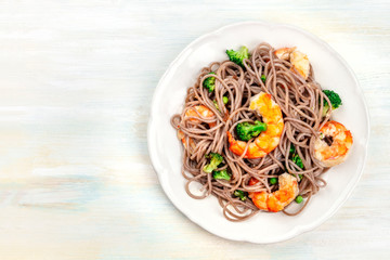A photo of cooked soba, buckwheat noodles, with shrimps and vegetables, shot from the top on a wooden background with copy space