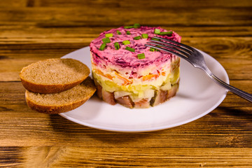 White plate with russian traditional new year salad herring under fur coat and rye bread on wooden table