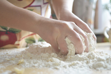 A woman in a colored apron kneads dough on the table.