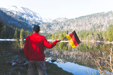 male hiker with red sweater is holding a german and an austrian flag in the mountains