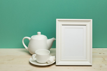 white frame with teapot and cup  on  desk near green wall