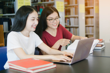 Young Asian woman using computer laptop with book in library or woman finding thesis book.Education Concept
