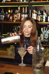 Professional bartender girl pouring a delicious cocktail into the glass at bar counter
