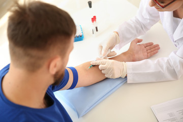 Female doctor drawing a blood sample of male patient in clinic