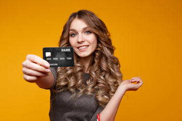 Portrait of a surprised happy girl holding shopping bags and showing credit card while looking at camera isolated over yellow background