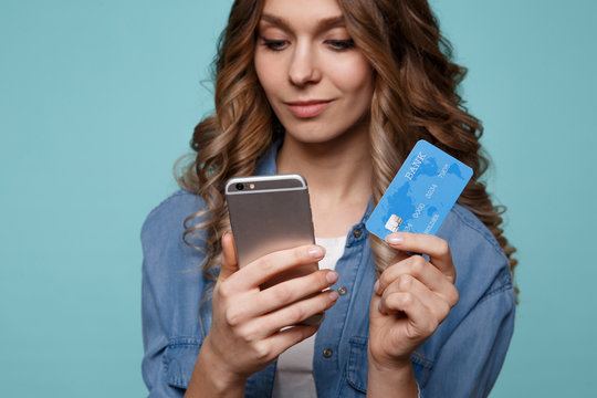 Image of excited young lady isolated over blue background using mobile phone holding credit card.