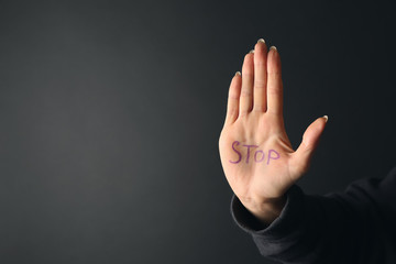 Word STOP written on palm of woman against dark background. Suicide awareness concept