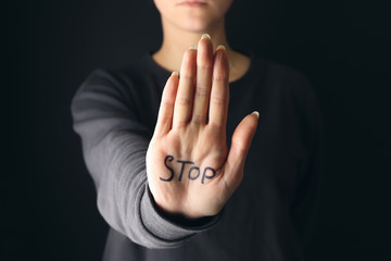 Word STOP written on palm of woman against dark background. Suicide awareness concept