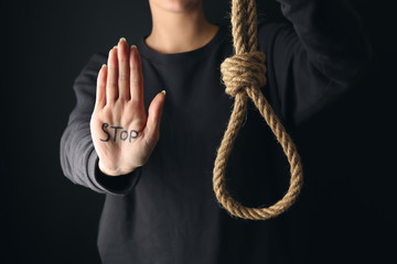 Fototapeta na wymiar Word STOP written on palm of woman and rope with noose against dark background. Suicide awareness concept
