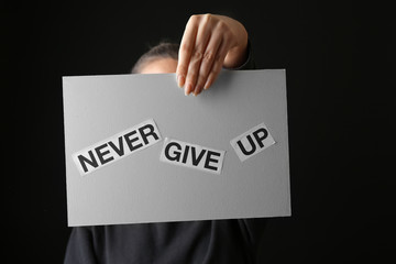 Woman holding paper sheet with text NEVER GIVE UP on dark background. Suicide awareness concept