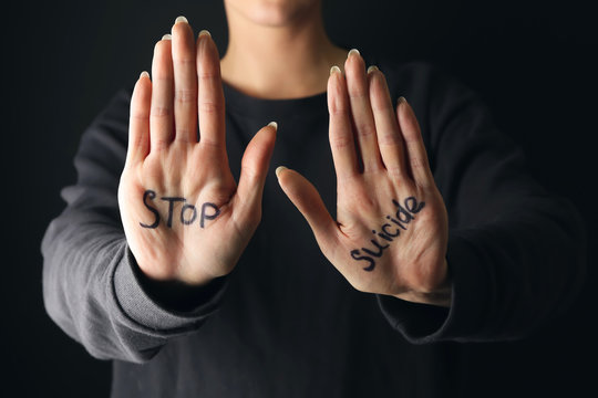 Text STOP SUICIDE written on palms of woman against dark background