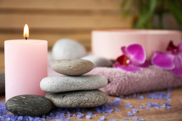 Burning candle with stones and sea salt on wooden table