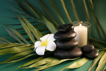 Beautiful spa composition with candle, stones and tropical flower on color background