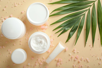 Jars of body cream and sea salt on color background